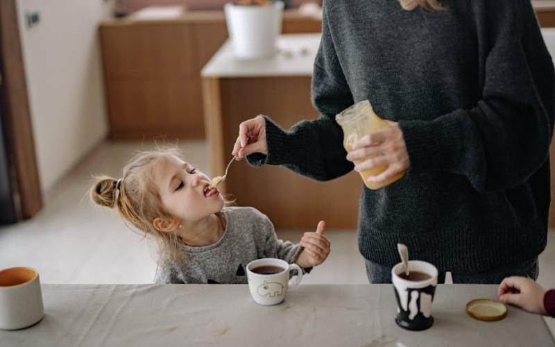 A child enjoys honey during a warm and cozy family breakfast with tea.