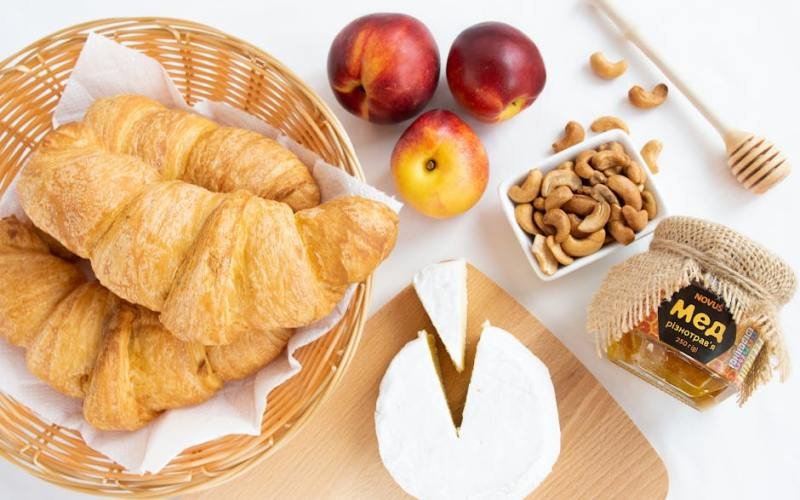 Flat lay of a French breakfast featuring croissants, camembert cheese, honey, and fresh fruits for a perfect start.