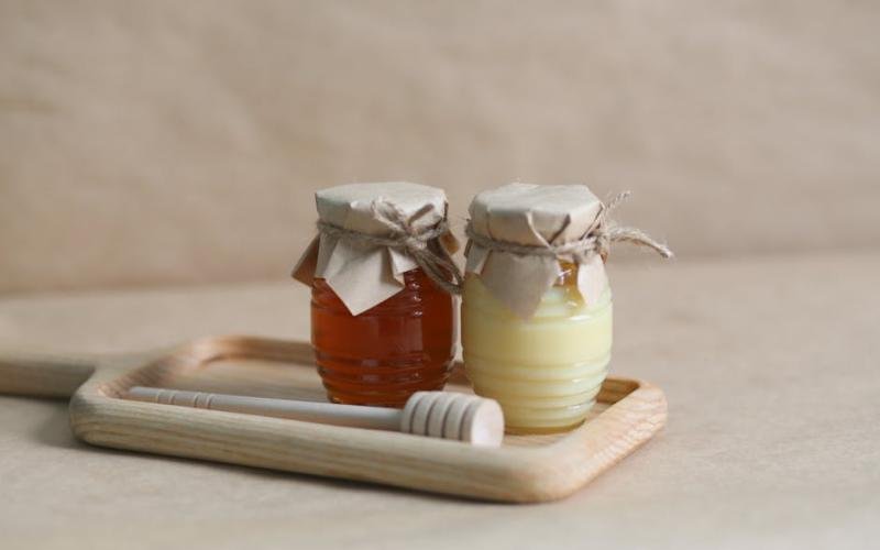 Two jars of honey on a wooden tray with a honey dipper, perfect for gourmet food styling.