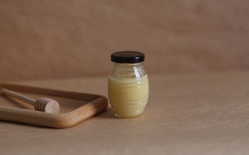 A glass jar of honey with a wooden dipper on a warm brown surface, offering an organic and homemade vibe.