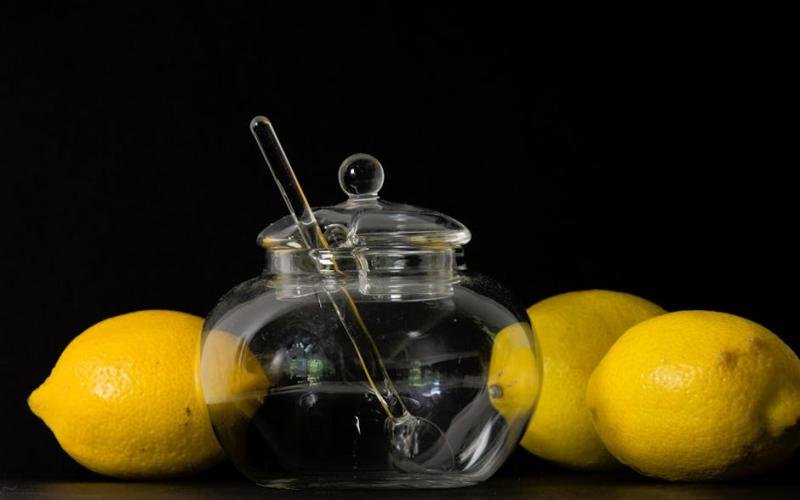 Elegant glass honey jar with lemons against a black background, showcasing a minimalist style.
