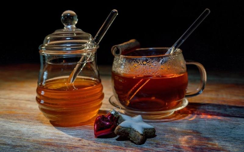 A warm glass of tea with honey and cinnamon on a wooden table, perfect for cozy winter relaxation.