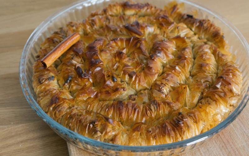 Close-up of freshly baked baklava in a glass dish with cinnamon stick.