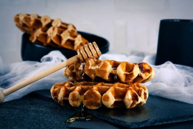 Tasty Belgian waffles drizzled with honey on a black plate, perfect for breakfast.
