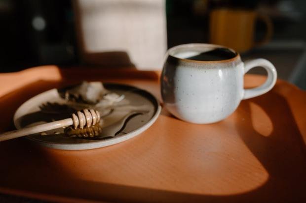 A cozy still life with a rustic tea mug and honey dip, bathed in warm sunlight.
