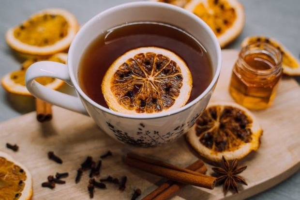 Close-up of a cup of tea with lemon slices, cinnamon, and honey on a wooden board.