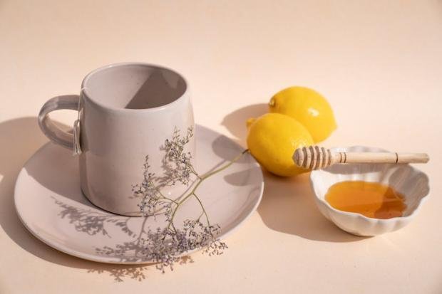 Aesthetic arrangement of a ceramic cup, lemons, and honey dipper for tea preparation.