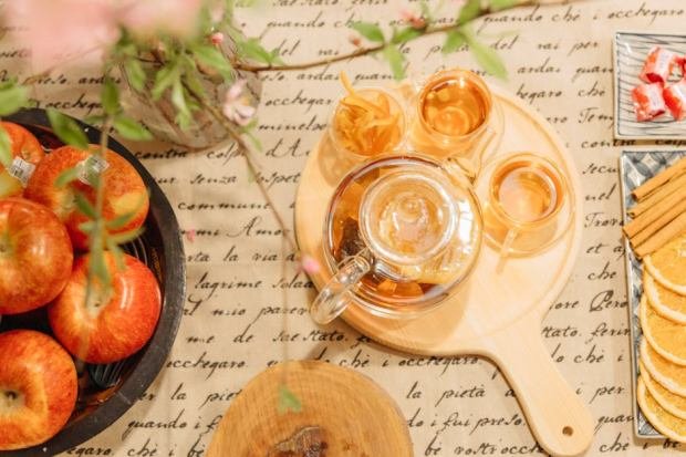 Elegant tea arrangement with fresh apples and spices on a script-patterned tablecloth.