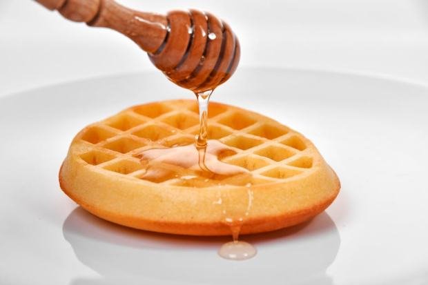 Close-up of honey being drizzled from a dipper onto a golden waffle on a white plate.