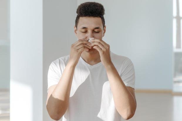 A man sneezing into a tissue, illustrating symptoms of flu or allergies.