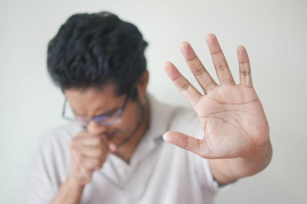 Unwell man covering cough with hand, showing sign of illness
