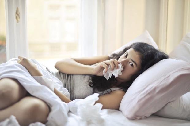 A woman lying in bed indoors, using tissue for cold and flu symptoms.
