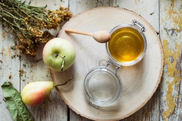 A rustic display of apple, pear, and honey with dried herbs on a wooden table setup.
