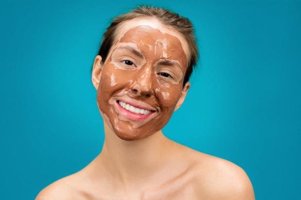 A woman smiles while wearing a moisturizing clay mud mask, enhancing facial care.