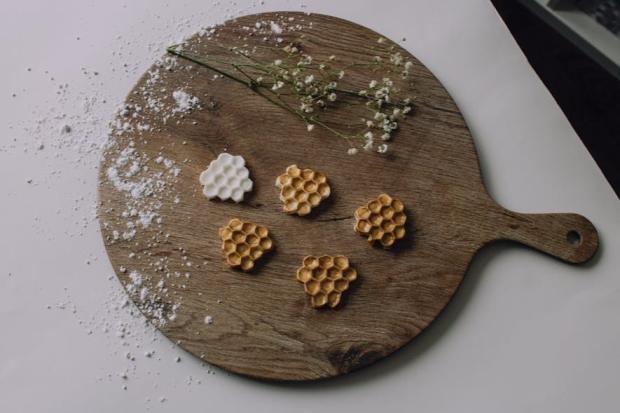Artistic display of honeycomb-shaped pastries on a rustic wooden board with floral garnish.