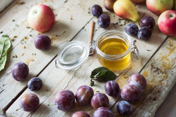 A rustic setup featuring apples, plums, pears, and honey jar on a wooden table.