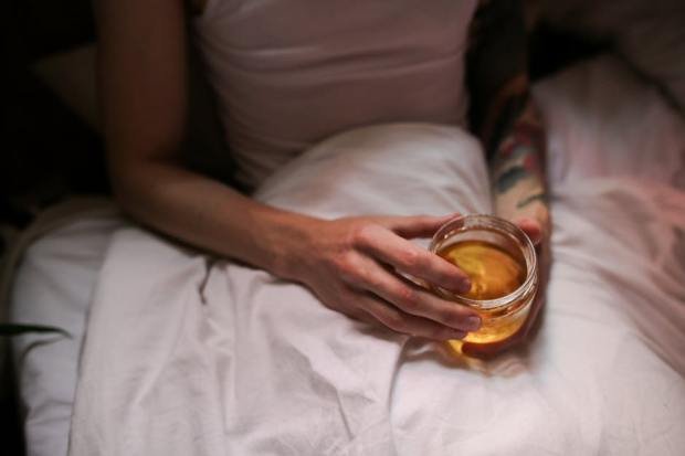 Close-up of a tattooed adult enjoying honey in bed, creating a cozy atmosphere.