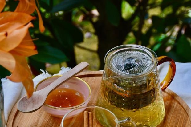 A warm herbal tea setup outdoors with honey, lemon, and flowers. Perfect for a cozy, nature-inspired experience.