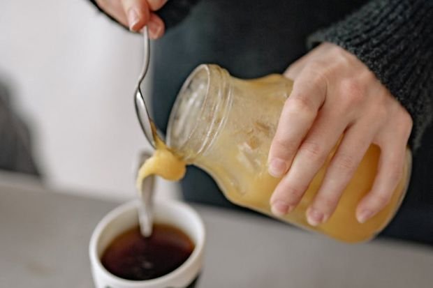 A person pours honey into a teacup, creating a warm, cozy atmosphere.