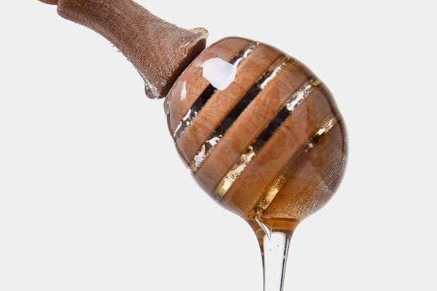 Sweet golden honey flowing from a wooden dipper, highlighting its thick, sticky texture.