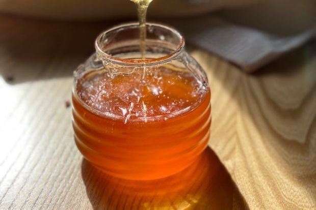 Close-up of honey drizzling into a glass jar on a wooden table, ideal for food and lifestyle themes.